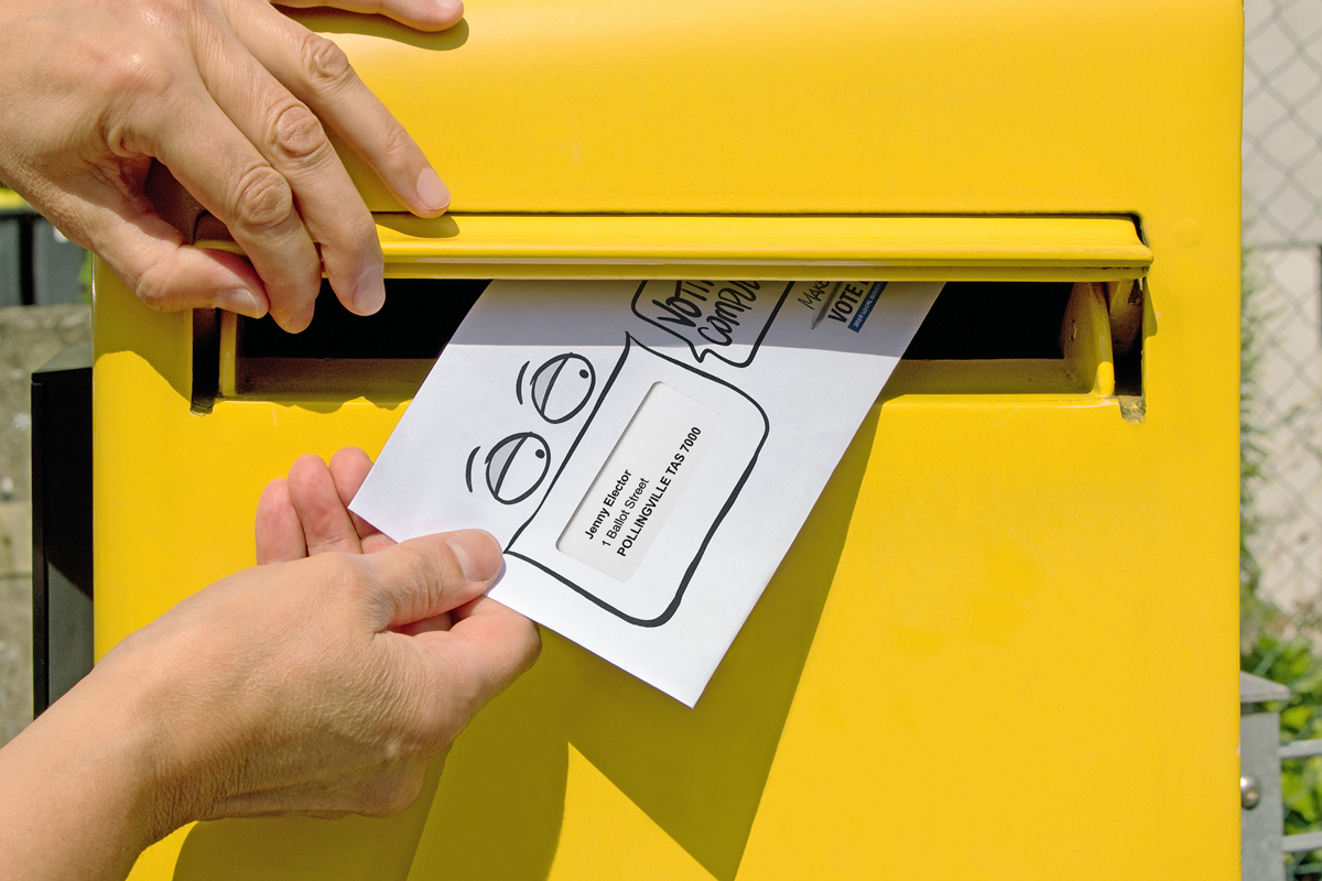 Close-up of hands opening a letterbox to deliver a postal ballot pack.